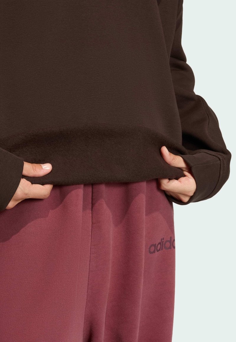 Brown sweatshirt with a soft texture and crew neckline, paired with maroon sweatpants featuring a subtle brand logo.