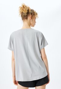 Blusa gris de mangas cortas y corte holgado con un escote redondo y detalles de costura sutiles; combinada con pantalones cortos negros, textura de tela suave.