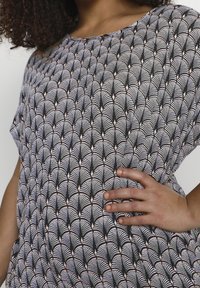 Haut noir et blanc présentant un motif de ventilateur, un col rond et une coupe ample. Le tissu a une texture lisse avec des accents roses subtils.