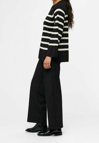 Top a strisce nero e crema con maniche larghe abbinato a pantaloni neri a vita alta e scarpe nere lucide. Fit sartoriale e morbido.
