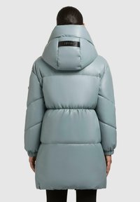 Puffet parka i lys blå med en stor hætte og elastiske manchetter. Har et taljebælte og en sort logoaccent på ryggen.