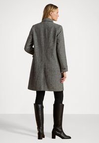 Sivý vlněný kabát s herringbone vzorom, po kolená, jednoradový strih, s výstrihom do "V", bočné vrecká, nosený cez čierne legíny a čižmy po kolená.