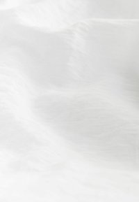 Tissu blanc, doux, avec une texture lisse et des vagues subtiles. Le matériau semble léger et translucide, présentant de légères variations d'épaisseur.