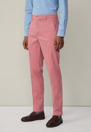 Pantaloni di cotone rosa con vestibilità slim e tasche frontali, abbinati a una camicia azzurra chiara e mocassini marrone scuro. Design a vita piatta.