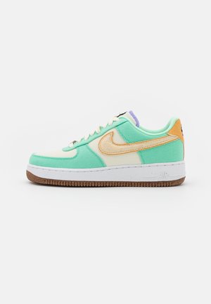 Niski sneaker w kolorze miętowo-zielonym i kremowym z beżowym logo Nike, fioletowym językiem, białymi sznurówkami, białą podeszwą środkową i brązową, teksturowaną podeszwą zewnętrzną.