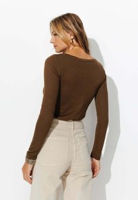 Chemise marron à manches longues, ajustée, avec un col rond, associée à un pantalon beige taille haute. Tissu simple et lisse sans motifs.