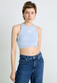 Light blue crop top in a stretchy fabric with a round neckline. Features a white logo at the center and a slim fit design. Paired with high-waisted denim.