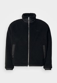 Čierna fleece bunda s vysokým golierom, zipsom, bočnými vreckami a rebrovanými manžetami. Obsahuje hladké textilné detaily na bokoch.