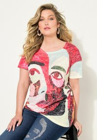 Camiseta multicolor con diseño de cara abstracta en rojo, negro y verde. Mangas cortas, escote redondo y textura de tela ligera.