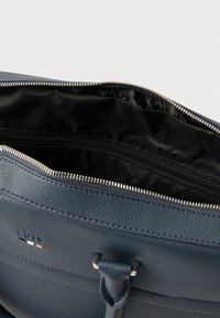 Nærbillede af en åben mørkeblå lædertaske, der viser sort stofindvendigt og sølvfarvede lynlåsedetaljer.