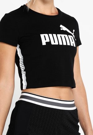 Frau trägt ein schwarzes Puma Croptop mit weißem Logo und schwarze Sportshorts mit gestreiftem Taillenbund.