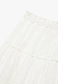 Falda blanca de capas hecha de tejido texturizado con una cintura fruncida, que presenta sutiles patrones florales en relieve y delicados acentos de decoración.