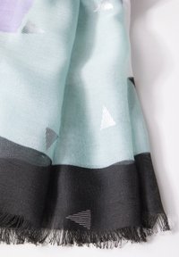 Écharpe tissée bleu clair et noire avec bords à franges et motifs triangulaires argentés et gris sur fond blanc.
