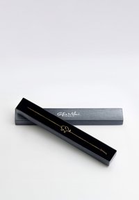 Ett guldarmband i form av en elefant, som visas i en svart smyckeslåda med en slät yta och varumärkesdetaljer på locket.