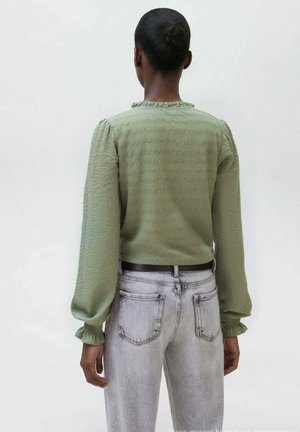 Maglietta verde chiaro a maniche lunghe con texture e spalle a palloncino, abbinata a jeans grigi sbiaditi a vita alta, con una cintura nera sottile.