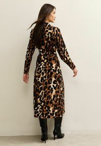 Leopardprint jurk van zacht materiaal, lange mouwen, taille cinched, enkel-lang, gecombineerd met zwart kniehoge laarzen.