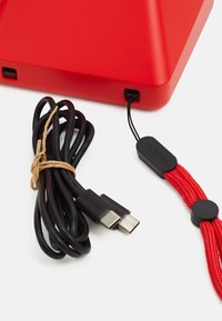 Red triangular device with matte finish, featuring a black USB charging cable, tied with natural twine, and a black clasp with red accents.