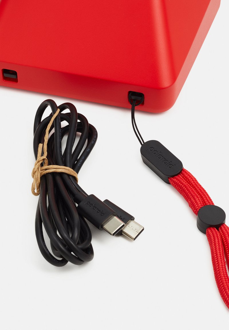 Red triangular device with matte finish, featuring a black USB charging cable, tied with natural twine, and a black clasp with red accents.