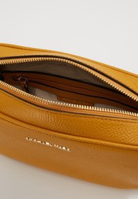 Gul tekstureret læder clutchtaske med lynlåslukning, der har et brunt interiør, en indre lomme og metallisk branding på ydersiden.