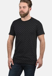 Schwarzes Kurzarm-T-Shirt aus Baumwolle mit einem weißen Punktemuster. Das Design hat einen Rundhalsausschnitt und eine reguläre Passform.