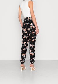 Pantalons floraux noirs avec des fleurs oranges et bleues, dotés d'une taille haute et de poignets élastiques aux chevilles, associés à un haut sans manches blanc.