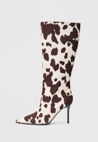 Botine cu vârf ascuțit până la genunchi, dintr-un material cu imprimeu de vacă crem și maro, având un toc stiletto subțire și o textură netedă.