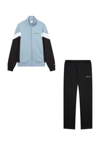 Chándal con chaqueta de cremallera azul claro que presenta paneles en negro y blanco, y pantalones negros a juego. Ambos artículos tienen acentos de logo.