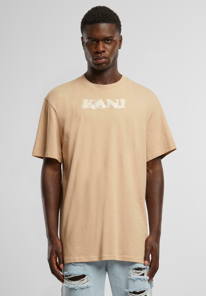 Beige cotton t-shirt with short sleeves, featuring a white "KANI" logo on the front. Pairing with distressed light blue jeans.