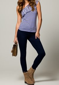 Pruhovaný top na jedno rameno v modré a bílé látce; spárovaný s námořnickými úzkými džíny a hnědými šněrovacími kotníkovými botami. Drží hnědou kabelku.