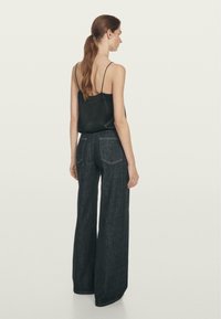 Czarny top na cienkich ramiączkach zestawiony z szerokimi spodniami dżinsowymi w ciemnym kolorze, z tylnymi kieszeniami i gładką, czystą fakturą.