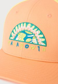 Καπέλο μπέιζμπολ σε ροδακινί χρώμα με κεντητό πολύχρωμο σχέδιο μισού ήλιου και γης και τη λέξη «Patagonia» σε κεντημένα γράμματα.