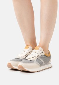 Gray and beige sneakers with a suede and felt texture, featuring a tan leather accent on the heel and cream-colored laces, retro design.