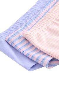 Tre foldede par børneunderbukser i pastelfarver: lavendel, pink med blå striber og lys gul med pink striber.