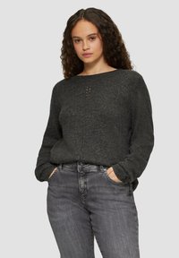 Dunkelgrauer Strickpullover mit Rundhalsausschnitt und dekorativen Frontdetails, kombiniert mit ausgewaschenen grauen Jeans, beide im lässigen Schnitt.
