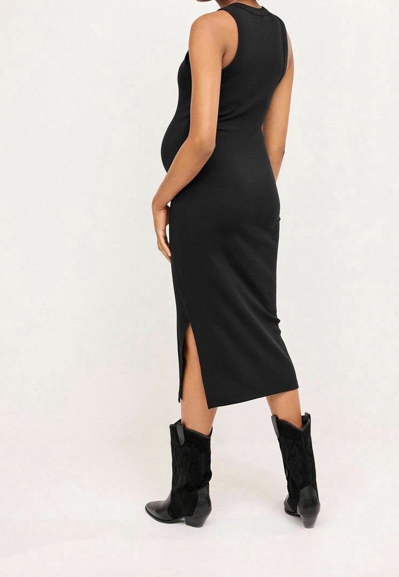 Mustasatamaton mekko, jossa on tiukka siluetti, sivuhalkiot ja sileä pinta, yhdistettynä mustiin cowboy-kenkäihin.