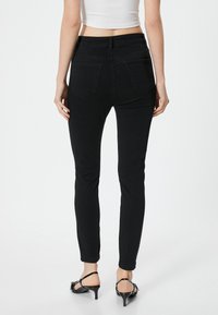 Jeans skinny de denim negro con cintura alta, dos bolsillos traseros y una textura suave. Combinados con tacones negros con tiras.