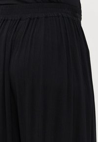 Pantalons larges plissés noirs avec une taille élastique. Tissu léger avec une finition texturée, conçu pour le confort et la liberté de mouvement.