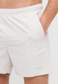 Biele plavky s elastickým pásom, bočnými vreckami a jemným šedým logom Calvin Klein na spodnej strane. Textúrovaná tkanina.