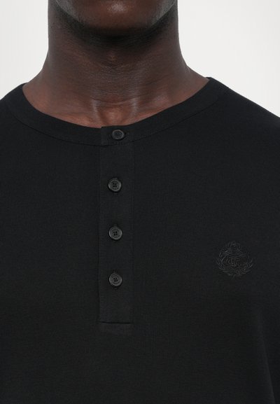 Čierna henley košela s okrúhlym výstrihom, so piatimi gombíkmi na prednej strane a jemne vyšitým logom na ľavej strane.