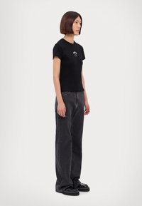 Svart bomulls t-shirt med korta ärmar och rund halsringning, med en liten vit grafisk bild på bröstet, matchad med mörkgrå vida jeans.