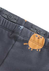 Grå stofshorts med legende orange og blå dyremønstre, elastisk talje med sort knapdetalje, glat tekstur.