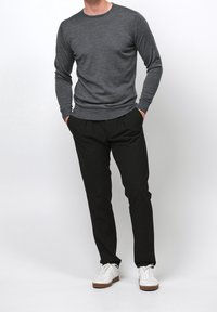 Grauer langärmeliger Pullover mit Rundhalsausschnitt und strukturierter Oberfläche, kombiniert mit schwarzen, locker sitzenden Hosen und weißen Sneakers.
