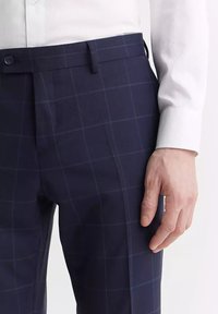 Granatowe spodnie w kratę wykonane z gładkiego materiału, o slim fit i zapinane na guzik w płaskim kroju z przodu.