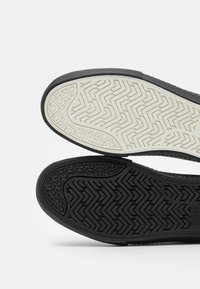 Plantillas de zapato en negro y crema, con patrones de espiga distintivos y superficies texturizadas para mejorar el agarre y la tracción.