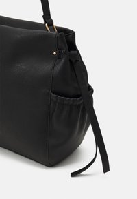 Černá kožená kabelka s texturovaným povrchem, boční kapsou a odnímatelným popruhem. Disponuje elegantním designem a minimálními zlatými akcenty.