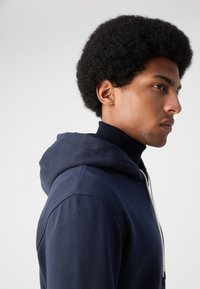 Sudadera azul marino con cordón y bolsillo canguro, hecha de una tela suave, con un acabado texturizado y un diseño casual y relajado.
