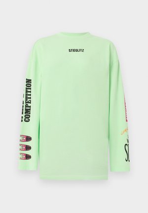 Chemise à manches longues vert clair avec le texte "STIEGLITZ" sur la poitrine et des textes graphiques noirs et colorés ainsi que des motifs sur les deux manches.