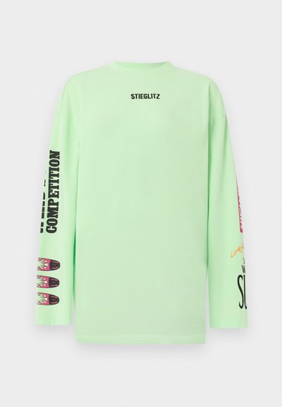 Μακρυμάνικο πουκάμισο ανοιχτού πράσινου χρώματος με το κείμενο "STIEGLITZ" στο στήθος και μαύρο και πολύχρωμα γραφικά κείμενα και σχέδια στα μανίκια και των δύο πλευρών.
