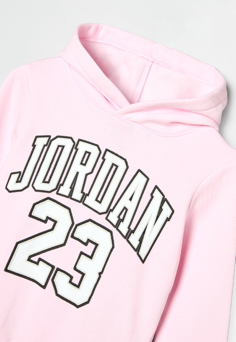 Haut à capuche rose clair avec cordon de serrage, arborant une grande écriture blanche "JORDAN" et le numéro "23" dans un motif texturé. Matériau en coton.
