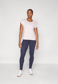 Világos rózsaszín, rövid ujjú póló lekerekített nyakkivágással, sötét tengerészkék leggingsszel párosítva. Az összeállítást fehér sportcipő egészíti ki.